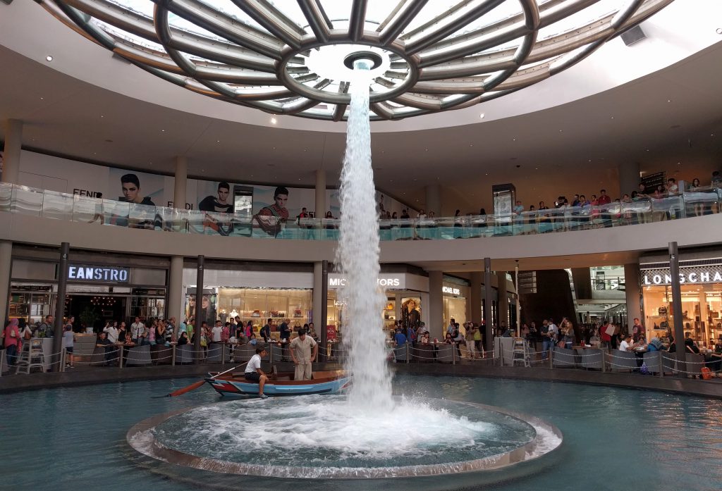 Der Wasserfall, der mit Regenwasser gespeist wird, befindet sich im Keller des Marina BaySadns Shopping Mall mit Cafés und Restaurants außenrum. wie man sieht kann man sich auf dem Wasser auch mit einem Boot herum fahren lassen.